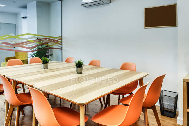 Простий творчий інтер'єр світлої сучасної кімнати зі зручними помаранчевими стільцями навколо великого дерев'яного столу проти білих і скляних стін — стокове фото