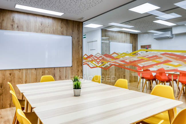 Modernes Interieur aus hellem, geräumigem Büro mit Glaswand, bequemen gelben Stühlen und grauen Barhockern an Holztischen — Stockfoto
