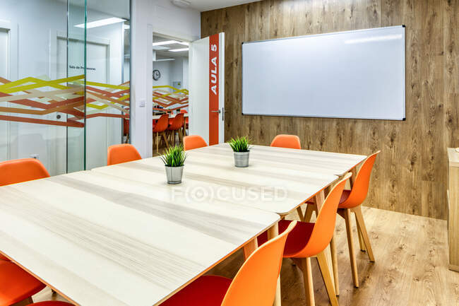 Modern interior design of light spacious office zoned by glass wall with comfortable orange chairs and gray bar stools at wooden tables — Stock Photo