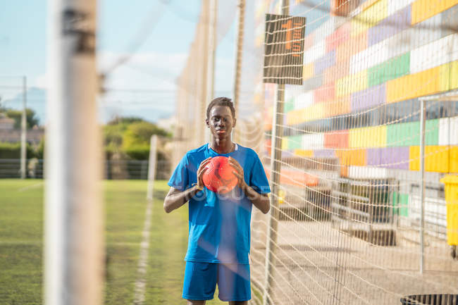 Черный подросток держит оранжевый на футбольном поле — стоковое фото