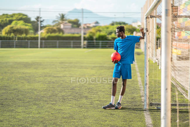 Black teenager leaning on goal post on football field — Stock Photo