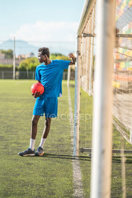 Adolescent noir penché sur le poteau de but sur le terrain de football — Photo de stock