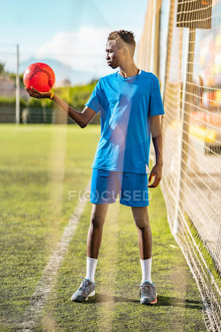 Preto adolescente segurando bola vermelha brilhante no campo de futebol — Fotografia de Stock