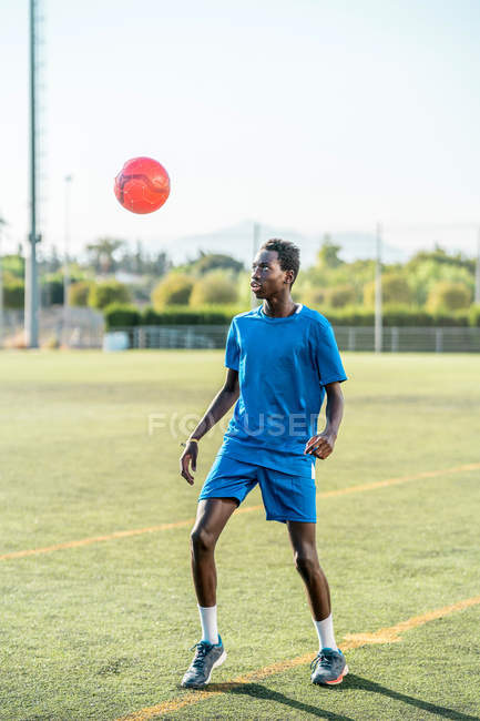 Черный молодой человек жонглирует футбольным мячом на зеленой лужайке — стоковое фото