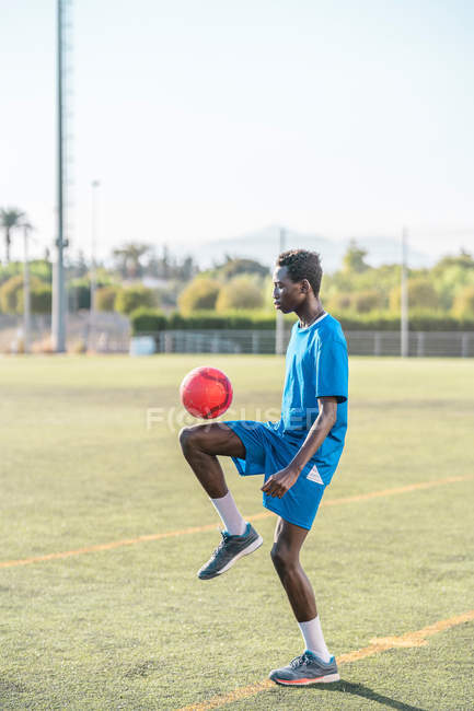 Schwarzer junger Mann jongliert mit Fußballball auf grünem Rasen — Stockfoto