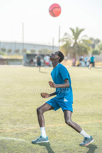 Skinny black teenager jugging football ball on head — Stock Photo