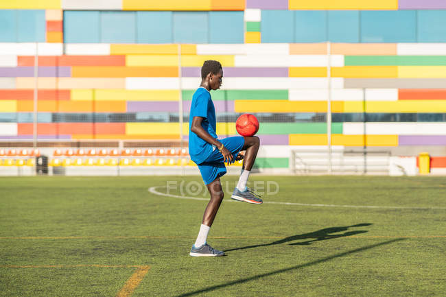 Ethnic male athlete juggling football ball on sport field — Stock Photo