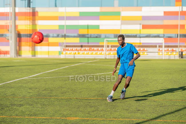 Athlète masculin ethnique jonglant avec le ballon de football sur le terrain de sport — Photo de stock