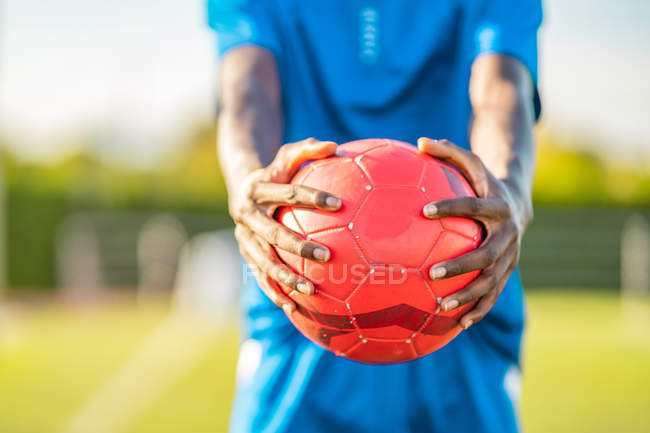 Руки черного футболиста в синей форме, несущего мяч — стоковое фото