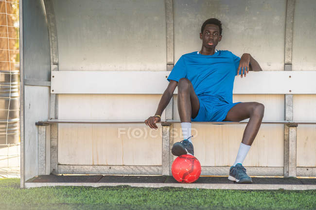 Черный футболист отдыхает на скамейке на поле — стоковое фото