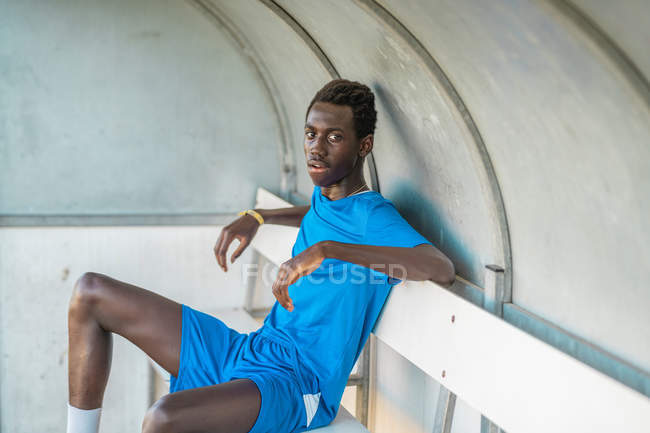 Schwarzer Fußballer ruht sich auf Bank auf dem Feld aus — Stockfoto