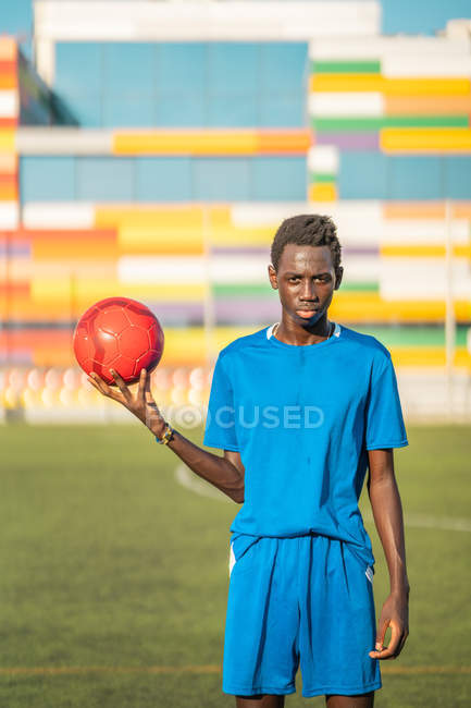Black teenager with football ball against stadium seats — Stock Photo