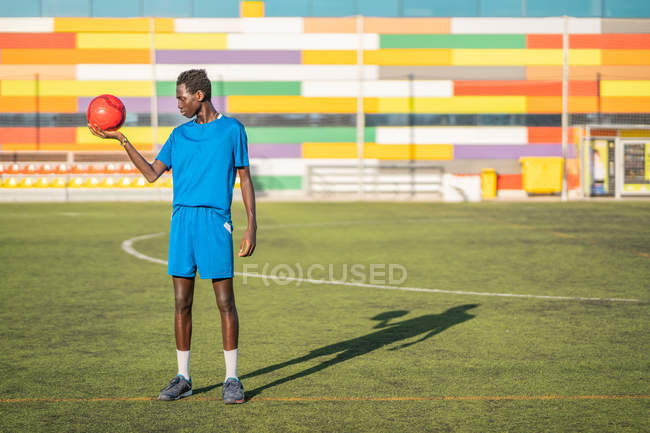 Черный подросток с футбольным мячом против мест на стадионе — стоковое фото