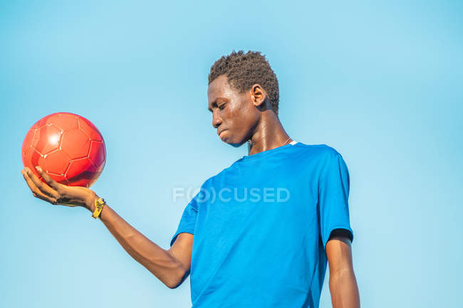 Black teenager holding red football ball against cloudless sky — Stock Photo