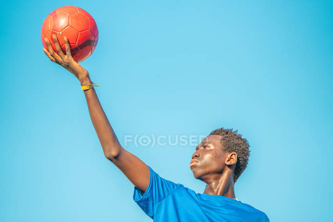 Черный подросток с футбольным мячом против неба — стоковое фото