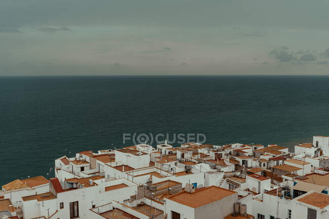 Aerial view of buildings with red roofs and on coast with dark water and grey cloudy sky — Stock Photo