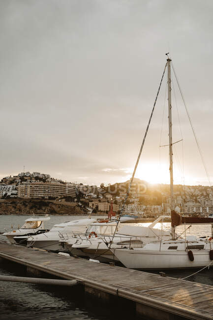 Sea port with white yachts and boats in city with buildings on hills at beautiful sunset with cloudy sky — Stock Photo