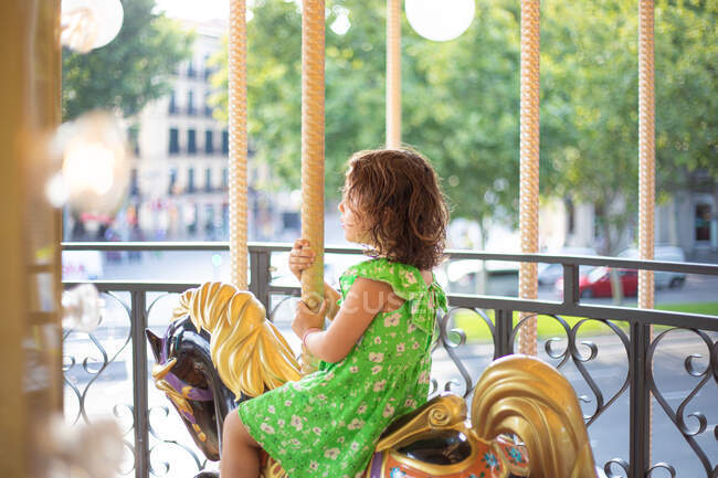 Charming little girl on colorful moving merry go round at fair in daylight — Stock Photo