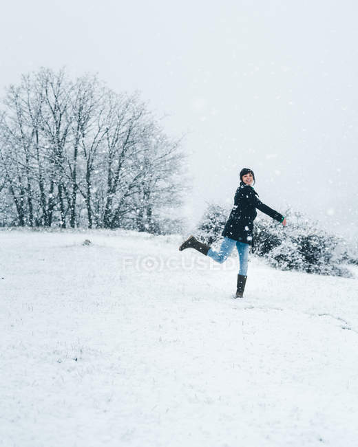 Vista lateral da mulher vestindo roupas quentes brincando com neve no campo de inverno com colinas — Fotografia de Stock