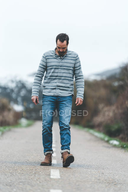 Homem adulto caminhando na estrada do país com colinas cobertas de neve em tempo nublado sombrio — Fotografia de Stock