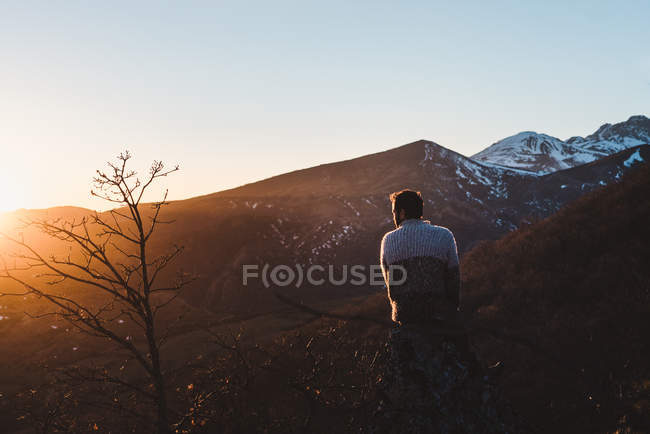 Вид ззаду на невпізнаваного чоловіка, що сидить на схилі гори на красивому осінньому заході сонця — стокове фото