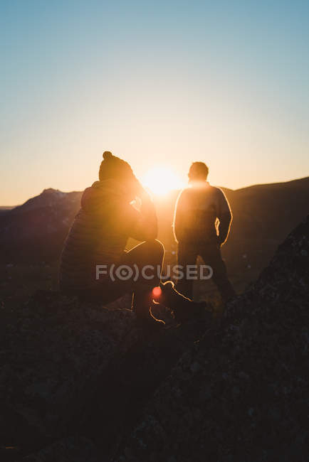 Silhouette of relaxed male and woman sitting in backlit on mountain top at sunset — Stock Photo
