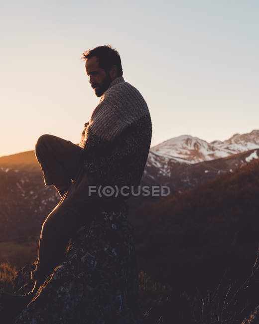 Side view of man sitting on mountain slope at beautiful autumn sunset with snowy peaks in distance — Stock Photo