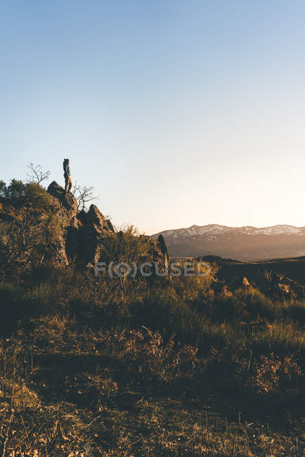 Vista lateral de la mujer joven en desgaste activo de pie en la pendiente de la montaña en el hermoso atardecer de otoño - foto de stock
