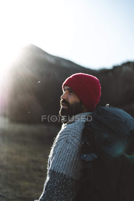Боковой вид на бородатого мужчину-туриста в красной вязаной шапке походы в горы в солнечную осеннюю погоду — стоковое фото