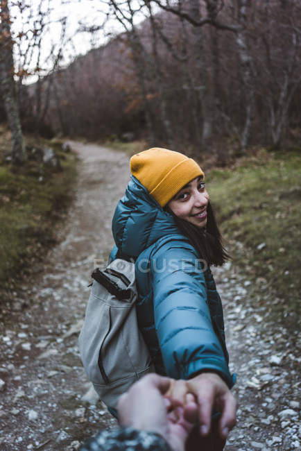 Девушка-подросток с рюкзаком тянет мужскую руку и приглашает на прогулку по тропе в осеннем лесу с лиственными деревьями — стоковое фото