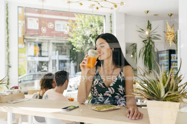 Senhora com bebida saudável ouvir música no café — Fotografia de Stock