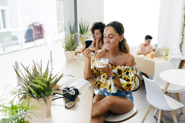Stilvolle Frau beim Essen und Lesen von Büchern im Café, Menschen im Hintergrund — Stockfoto