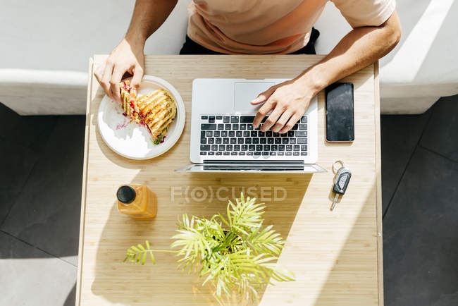 Vista superior do homem desfrutando de sobremesa doce e laptop de navegação enquanto está sentado à mesa no restaurante moderno — Fotografia de Stock