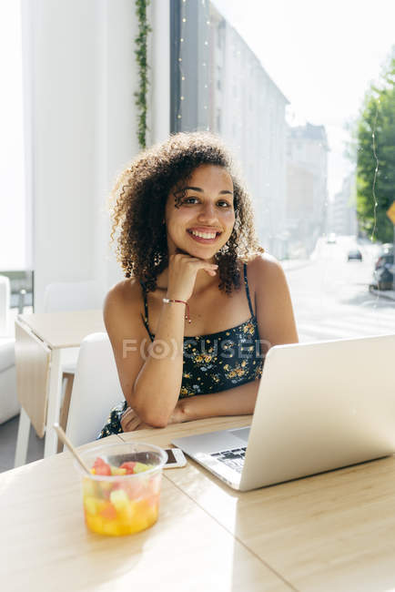 Mulher sorrindo e olhando na câmera como usar laptop no café — Fotografia de Stock
