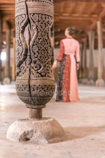 Coluna de madeira com majestoso ornamento oriental esculpido em Mesquita de Juma com mulher borrada em roupas tradicionais de pé e olhando para longe — Fotografia de Stock