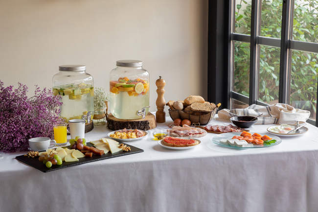 Vue latérale du dîner festif avec de savoureux fruits, des pâtisseries et des bancs de limonade élégants sur une table décorée de fleurs de lilas — Photo de stock