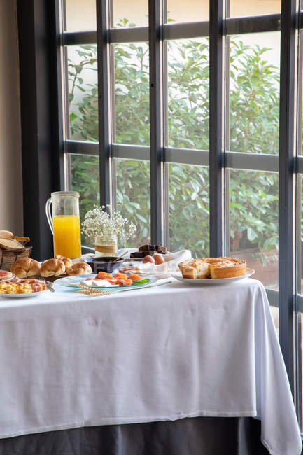 From above of appetizing sitting table for breakfast with bakery seafood sandwiches eggs and orange juice at stylish dinning room. — Photo de stock
