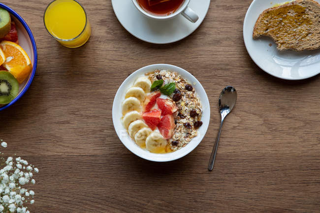 From above bowl of granola with tasty berries and banana served on table with plate of fruit and tea cup with for breakfast — Stock Photo