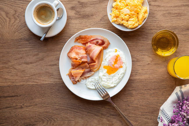Von oben frische Spiegeleier mit Speck im Teller serviert auf dem Tisch mit Saft und Kaffee zum Frühstück — Stockfoto