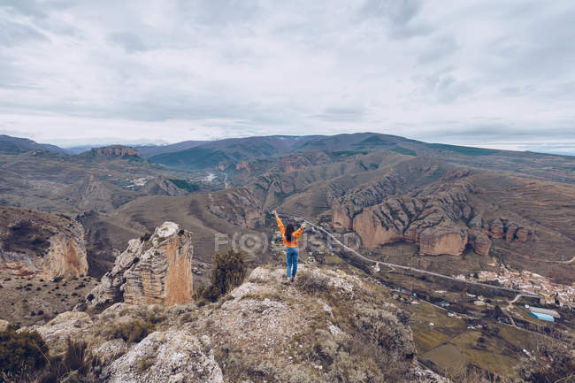From behind joyful woman in bright clothes standing with hands up at mountain top — Stock Photo