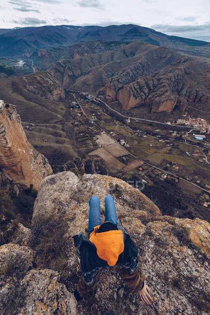 Вид сверху на неузнаваемую женщину, сидящую на скалах на краю скалы с живописным видом — стоковое фото
