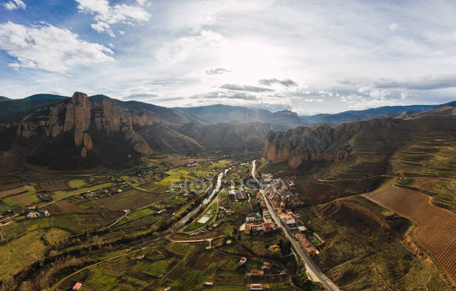Drone vista de pintorescas laderas de montañas cubiertas de hierba y campos con infraestructura en el valle - foto de stock