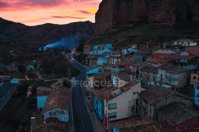 Modern buildings with tiled roofs by road next to rocky cliff in twilight — Stock Photo