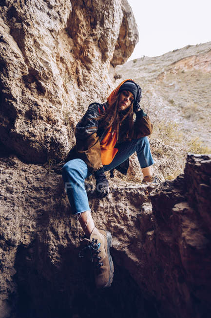 Спокійна жінка в теплому одязі спирається на руку і сидить на гірській скелі — стокове фото