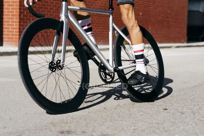 Обрезанное изображение велосипедиста в спортивной одежде и солнцезащитных очках на велосипеде возле красной кирпичной стены — стоковое фото