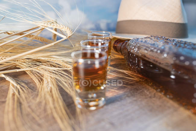 Uísque tiros com chapéu e trigo na mesa rústica — Fotografia de Stock