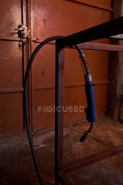 Сварочная горелка висит на металлической раме в мастерской с металлической дверью на заднем плане — стоковое фото