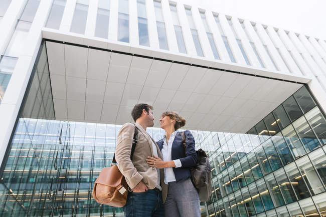 From below happy couple coworkers looking at each other while standing outside modern building on city street after work — Stock Photo