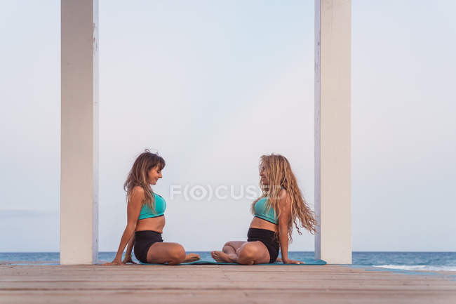 Sorridente donne sedute e stretching in farfalla postura al mare — Foto stock