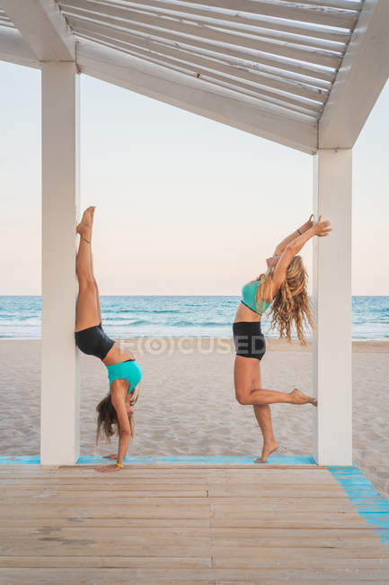 Side view of active sportive women preparing and performing acroyoga first hollowback handstand — Stock Photo